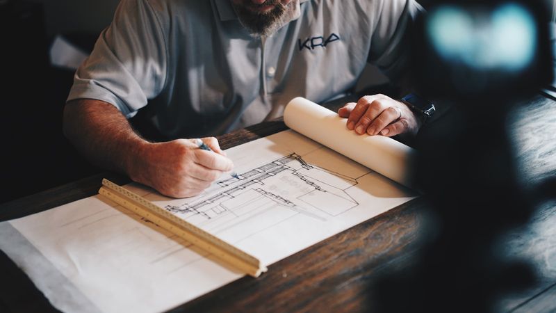 An architect drafting a technical plan with a pencil and ruler on white paper, seen from above
