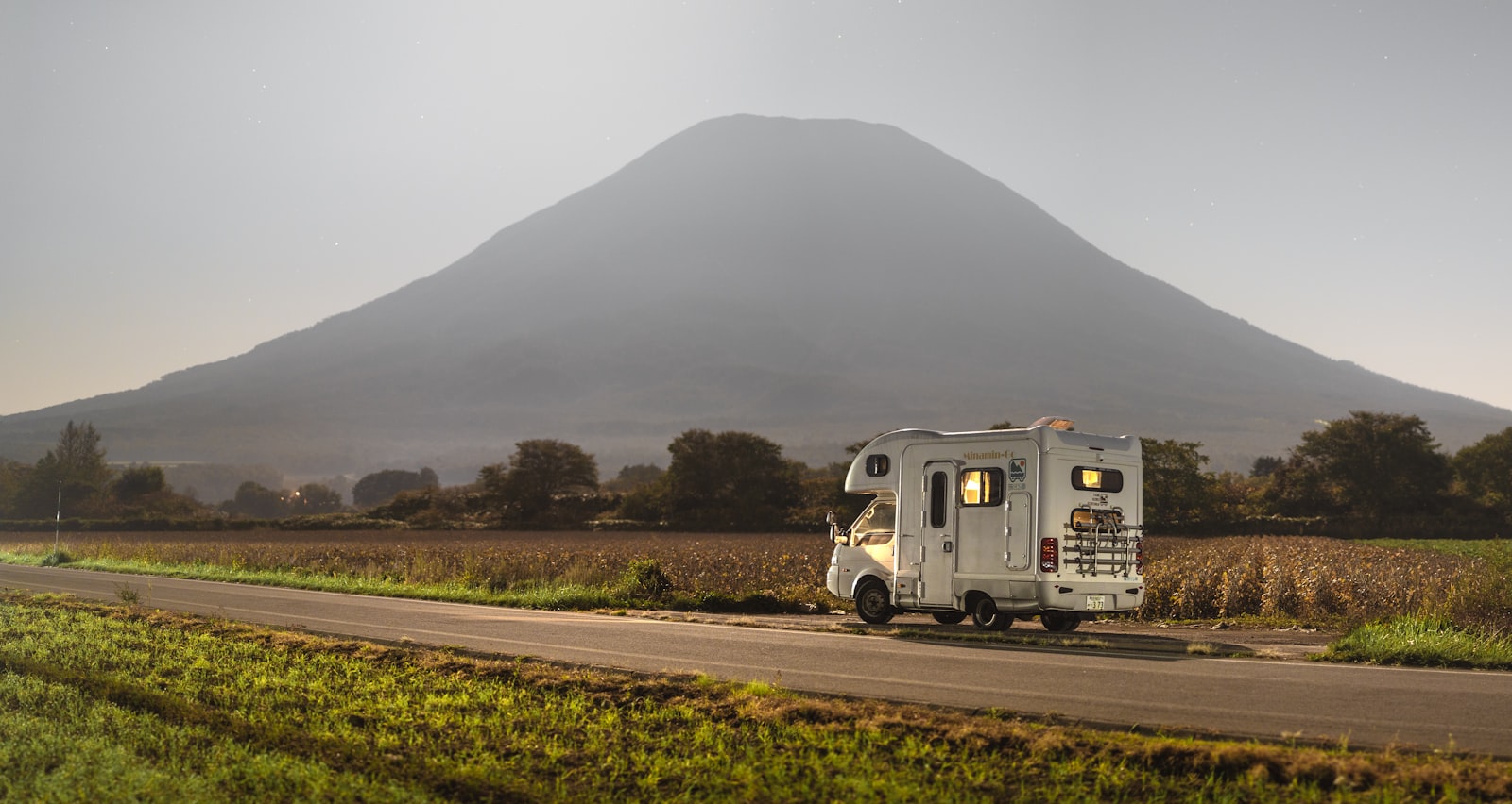 A small campervan on a rural road at twilight beneath a perfectly conical mountain — the kind of place cell coverage runs out and offline maps start mattering